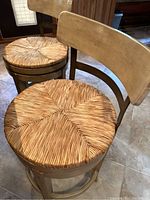View showing close up of one chair's woven rattan seat and light wood backrest, illustrating material and condition including visible scratches.