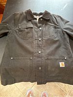 Front view of black Carhartt ladies jacket showing button closure, chest and lower pockets, and logo patch