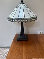 Front view of one table lamp showing stained glass shade and dark brown base on wooden surface against wall.