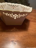 Close-up showing the white crystal bowl with delicate floral cutout pattern and gold trim on the scalloped rim.