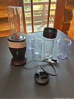 Full view of the Ninja Bullet blender with four clear blending cups, black blending lid, and power base with cord on a table.