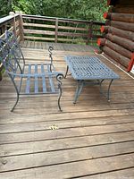 Photo showing two-person metal loveseat and rectangular metal table on wooden deck outdoors.