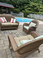 Overall view of three-piece rattan patio furniture set around an outdoor pool showing seating arrangement and cushions.