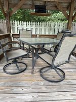 Full view of the patio set showing glass-top table with four matching swivel chairs around it.