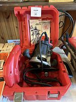 Milwaukee router inside red carrying case with instruction manuals and packaging inserts visible behind.