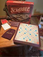 Photo of deluxe Scrabble game set including game board, tiles, tile racks, timer, score pads, and pouch laid out on table with box in background.