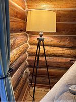 Full view of standing floor lamp with tripod prong legs and off-white cylindrical shade.