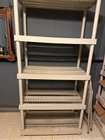 Front view of one tan plastic storage shelving unit with three open grid shelves, showing vertical supports and spacious shelf surface.