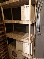 Front view of the tan stackable plastic shelving unit with three visible shelves and some boxes on lower shelves.