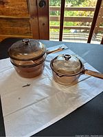 Two brown transparent glass cookware pieces on a blue table with visible outside scenery.