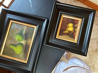 Two framed hand painted paintings of pears, one with green pears and one with yellow pears, both in dark wood frames with gold accents, laid on floor for photo.