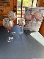 Three rose gold crafted glass candle holders with cracked glass design and retail packaging box behind them.