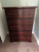 Front view of the wooden dresser showing five closed drawers with round knobs.