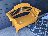 Front side view of the yellow painted antique bench showing curved spindled backrest and armrest details.