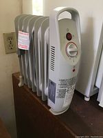 Side view of white oil-filled mini heater with four fins and control panel visible.