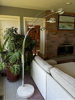Full view of the metal 5-light floor lamp positioned next to a couch and potted plant, showing the curved arms and dome-shaped light fixtures.