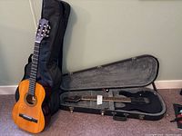 Both guitars displayed together: acoustic in padded gig bag standing upright, electric in open hardshell case.
