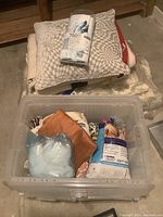 Photo of decorative pillows, assorted fabric and packaged shower curtain stored in a plastic bin.