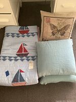Quilt folded with all three items visible: quilt and two pillows, showing sailboat designs, butterfly motif pillow and solid pillow.