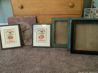 Photo showing two framed seed art prints (Watermelon and Tomato) and three empty shadow boxes in different colors, with a distressed red clock in background.