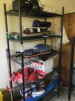 Black metal wire rack partially assembled showing multiple shelves with sports and utility items on and around it.