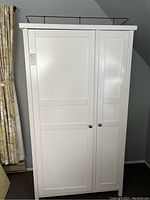 Front view of white wardrobe with two panel-design doors and black metal knobs.