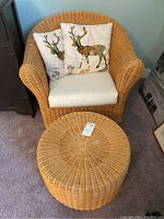 Wicker chair with white cushion and two decorative pillows featuring deer designs, plus matching wicker ottoman.