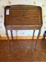 Front view of wooden writing desk with drop leaf closed, showing brass lock detail and curved legs.