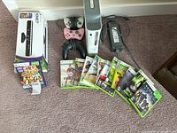 Xbox 360 console, Kinect sensor box, two controllers, power adapter, and stacked games on carpet