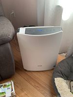 Angled view showing air purifier plugged in and operating with blue LED on display.