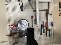 Wide view of pegboard with two metal framing squares and several hand tools hung, plus mounted 12 inch circular saw blades in packaging.
