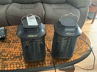 Two electric Tusonia bug lights on a wooden table, showing full units including cords and handles.