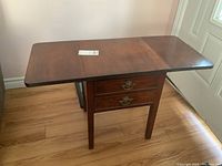 Front view of the wooden drop leaf table showing both leaves extended and two drawers beneath tabletop with metal handles.