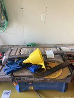 View of the Mastercraft electric tile saw with attached yellow blade and accessories on top including blue Allen key holder, yellow funnel, and small pry bar.