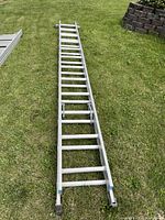 Full length view of the 24 ft aluminum extension ladder laying flat on the grass, showing both sections.