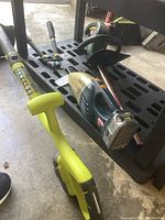 Yardworks handheld vacuum, Ryobi string edger, Yardworks hedge trimmer, and loppers arranged on a garage floor