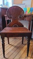 Front view of the solid mahogany George III style hall chair showing the carved ornate backrest and square seat with scratches and paint residue
