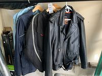 Photo of four jackets hanging on racks including two Wetskins rain suits, one motorcycle jacket with inserts, and one Milwaukee Leather jacket
