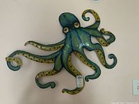 Photo of blue-green-yellow metal octopus wall decor with curled tentacles and eyes on a white wall