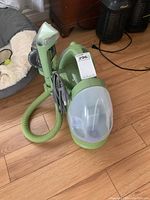 Side view of portable green Bissell Little Green rug cleaner with hose attachment and transparent water tank.