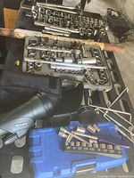 Overview of two socket sets in molded plastic cases with various sockets and extension bars laid out, alongside a green SKY monocular telescope in a black carrying pouch.