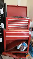 Front view of red Mastercraft tool chest with open hinged lid revealing content, top section with four drawers, bottom cabinet with two drawers and metal door, slightly dusty and used condition