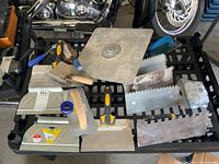 Photo showing various trowels including large flat trowel, notched trowels and grout floats arranged on a plastic shelf.