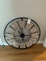 Front view of large wall clock showing metal frame and wooden number plaques mounted with large metal numerals from 1 to 12.