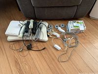 Overview of Nintendo Wii console, remotes, nunchucks, balance board, sensor bar, and game discs with cases laid out on floor.