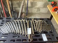 Full view of two sets of wrenches laid out on a black perforated work bench, showing all sizes and polished finish.