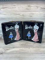 Two vintage black vinyl Barbie carrying cases side by side with illustrated Barbie in red gown and smaller blue tutu doll on front.