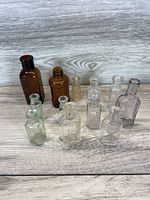 Eleven antique glass medicine bottles of various sizes and colors displayed on a wooden surface.