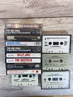 Top down photo showing eight cassette tapes and two blank cassette shells in plastic cases, displaying the exposed cassettes and labels confirming titles and condition.