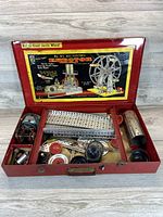 Open vintage Gilbert Erector Set box showing metal beams, wheels, gears, motor, and construction pieces.